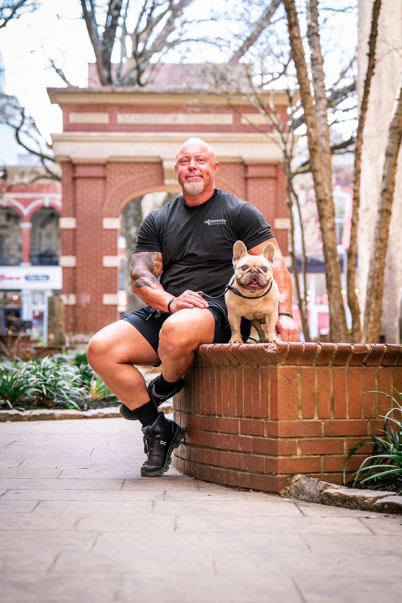Justin Rigney, head dog trainer at K9 Services Unlimited, seated on a brick ledge with a small dog