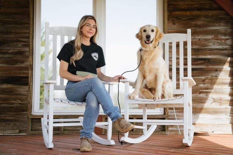 Woman sitting on a white rocking chair with a yellow Labrador on another chair on a porch