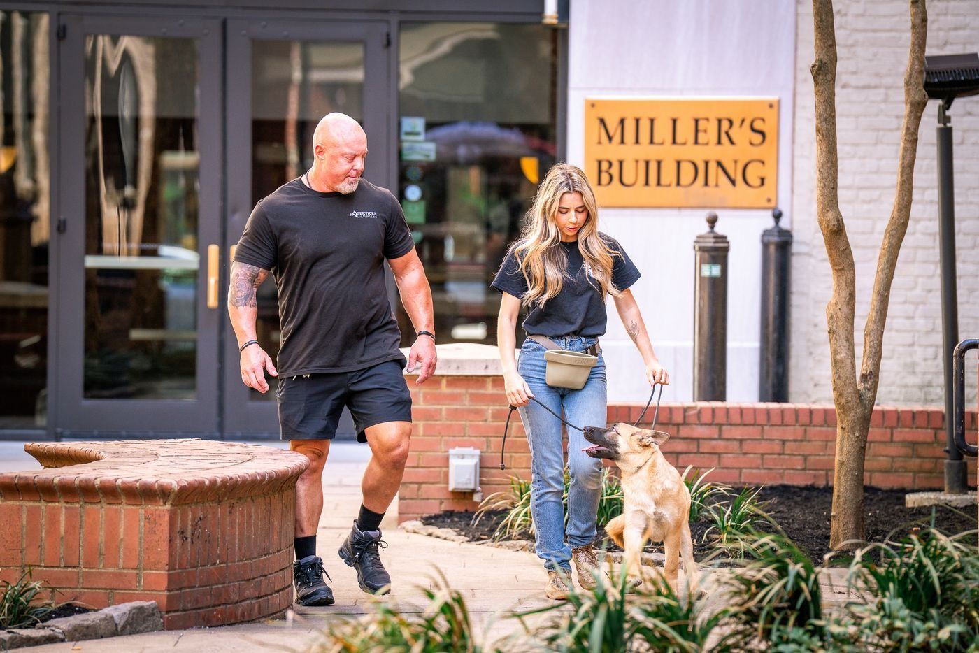 Two people walking a dog outside Miller’s Building entrance
