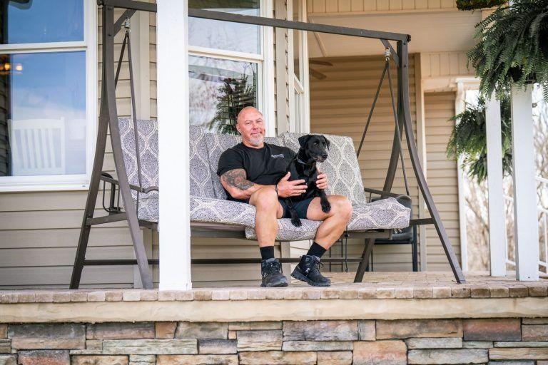 Trainer relaxing on a front porch swing with a calm black dog, Knoxville dog behavior training