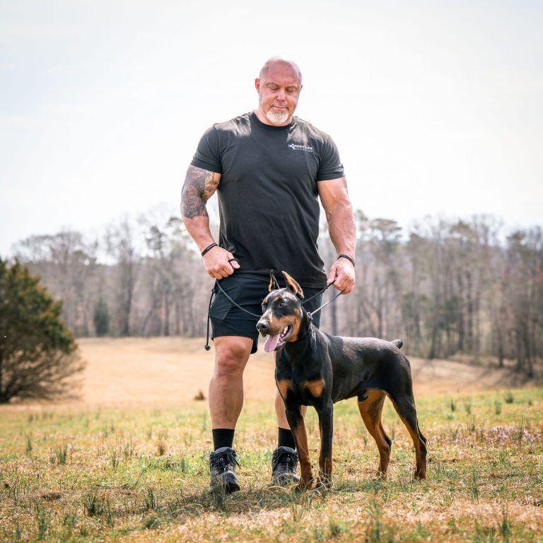 K9 Services Unlimited trainer standing with a leashed Doberman in an open field near Knoxville, TN