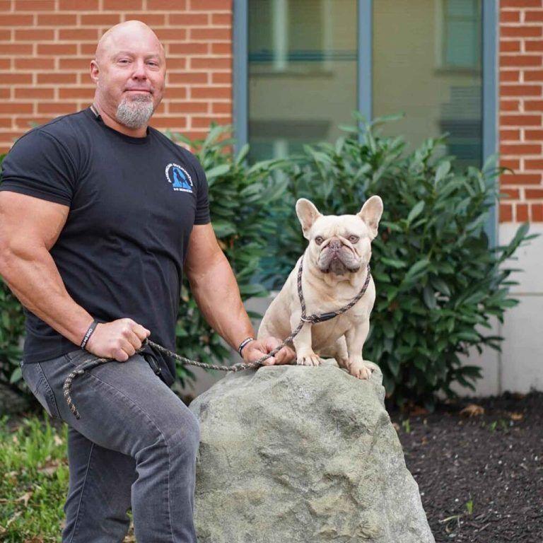 Justin Rigney with a French bulldog sitting on a rock in front of a brick building, Knoxville dog trainer