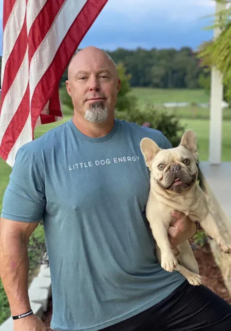 Justin Rigney, Knoxville dog trainer, holding a cream French bulldog in front of an American flag