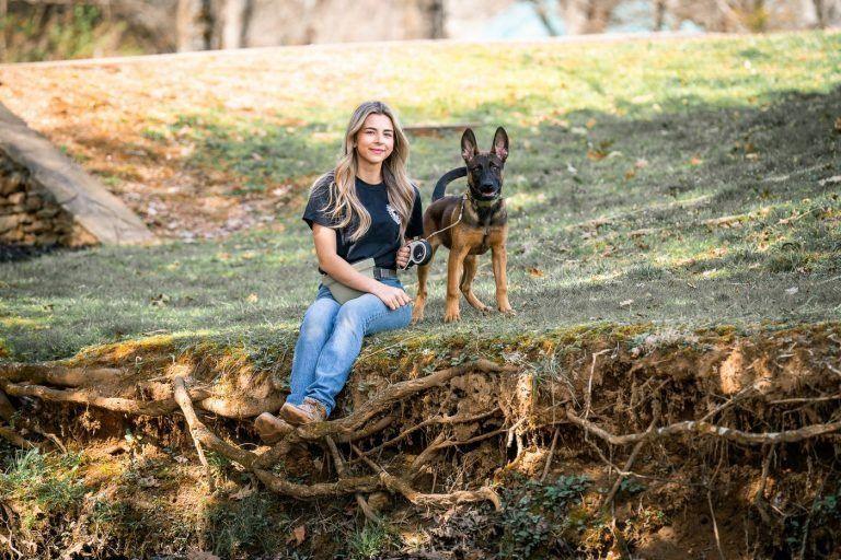 Trainer sitting on a grassy creek bank with a young German Shepherd, Knoxville puppy and young dog training