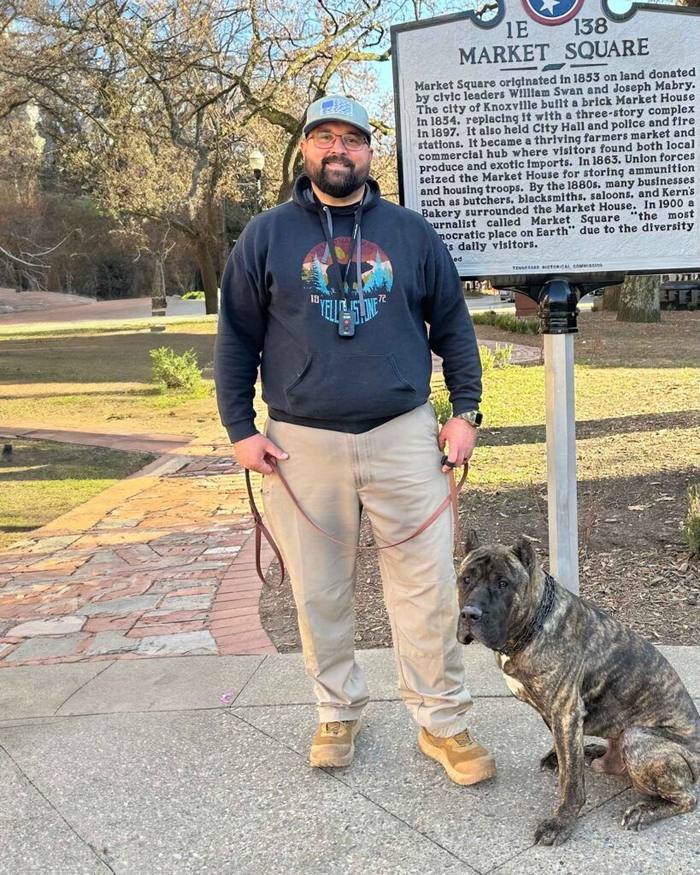 Man standing by a market square sign with a seated dog