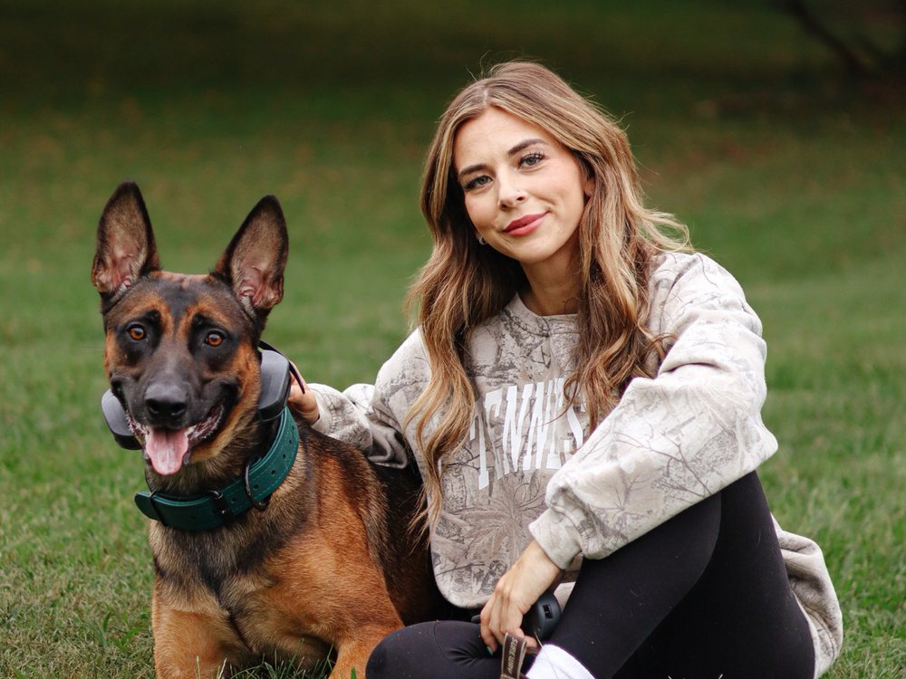 Rebeka, dog trainer at K9 Services Unlimited, sitting in the grass with her dog