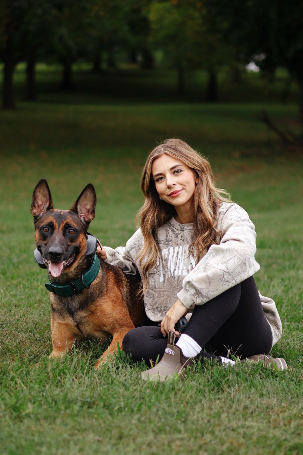 Rebeka, dog trainer at K9 Services Unlimited, sitting in the grass with her dog in a park