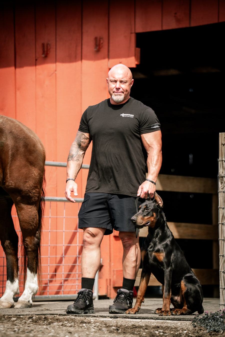 Justin Rigney, founder and head trainer, standing with a Doberman in front of a red barn