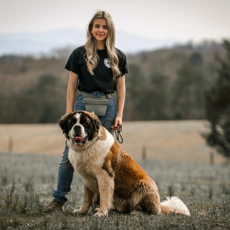 Rebeka standing with a Saint Bernard on a hillside farm